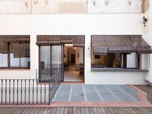 Outdoor patio with metal railing, wooden deck, and large windows with bamboo shades, leading into a modern interior.