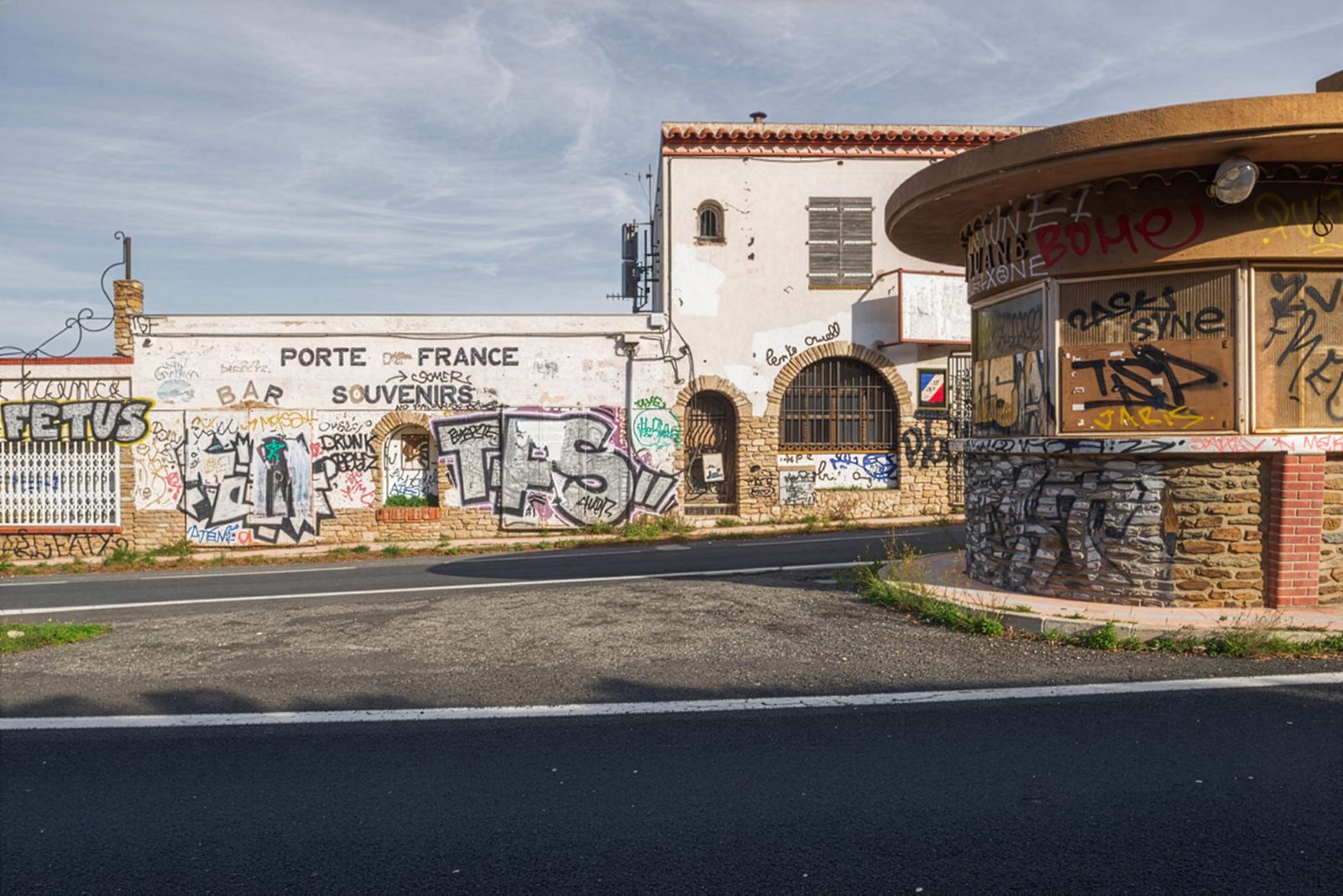 Un edificio abandonado con 'Porte de France, Souvenirs' escrito en la pared, cubierto de graffiti frente a una carretera vacía.