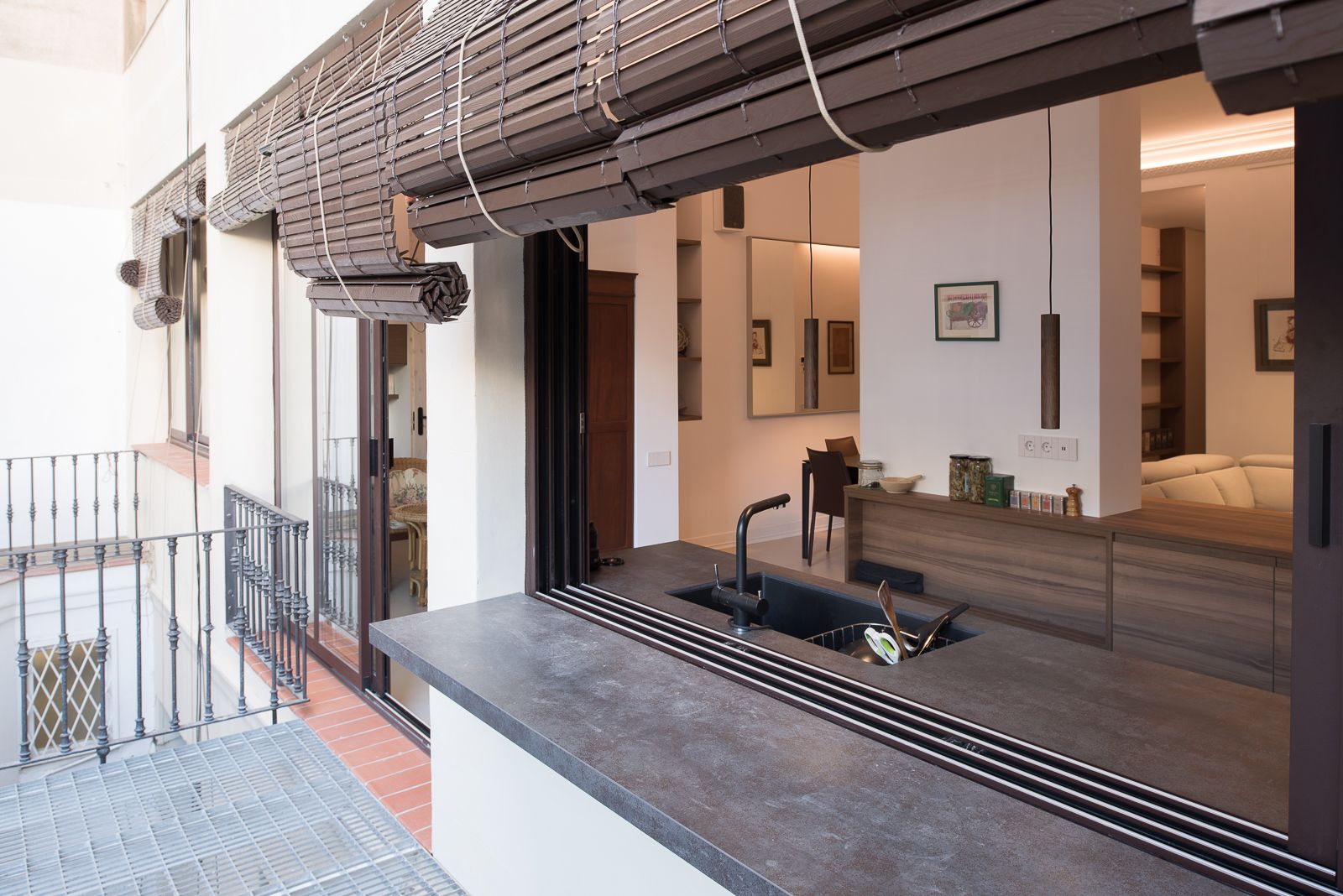 Modern kitchen with an open window bar to the outdoor terrace, featuring a sleek countertop and rolled-up blinds.