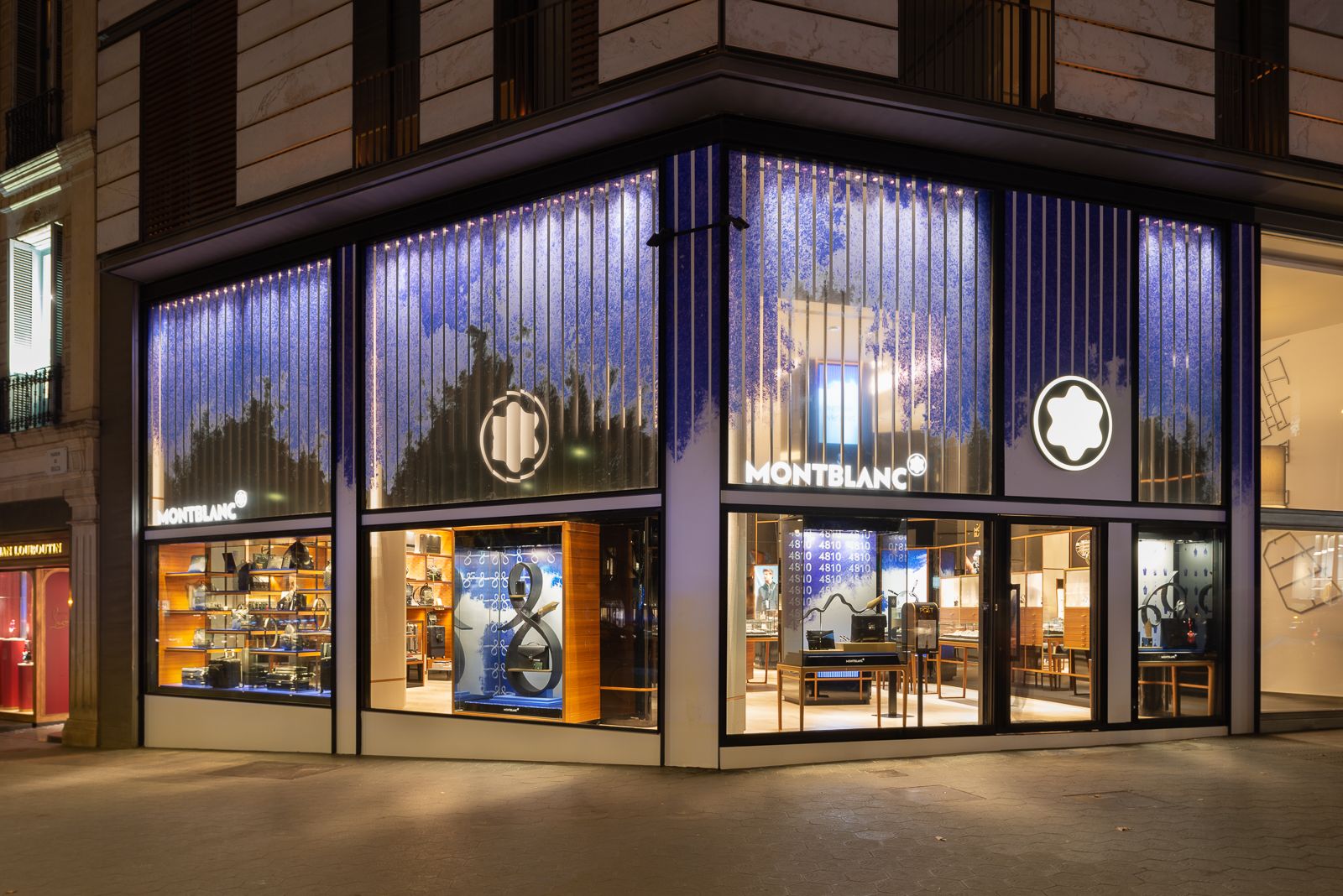 Montblanc store exterior at night with illuminated windows showcasing products and artistic blue design.