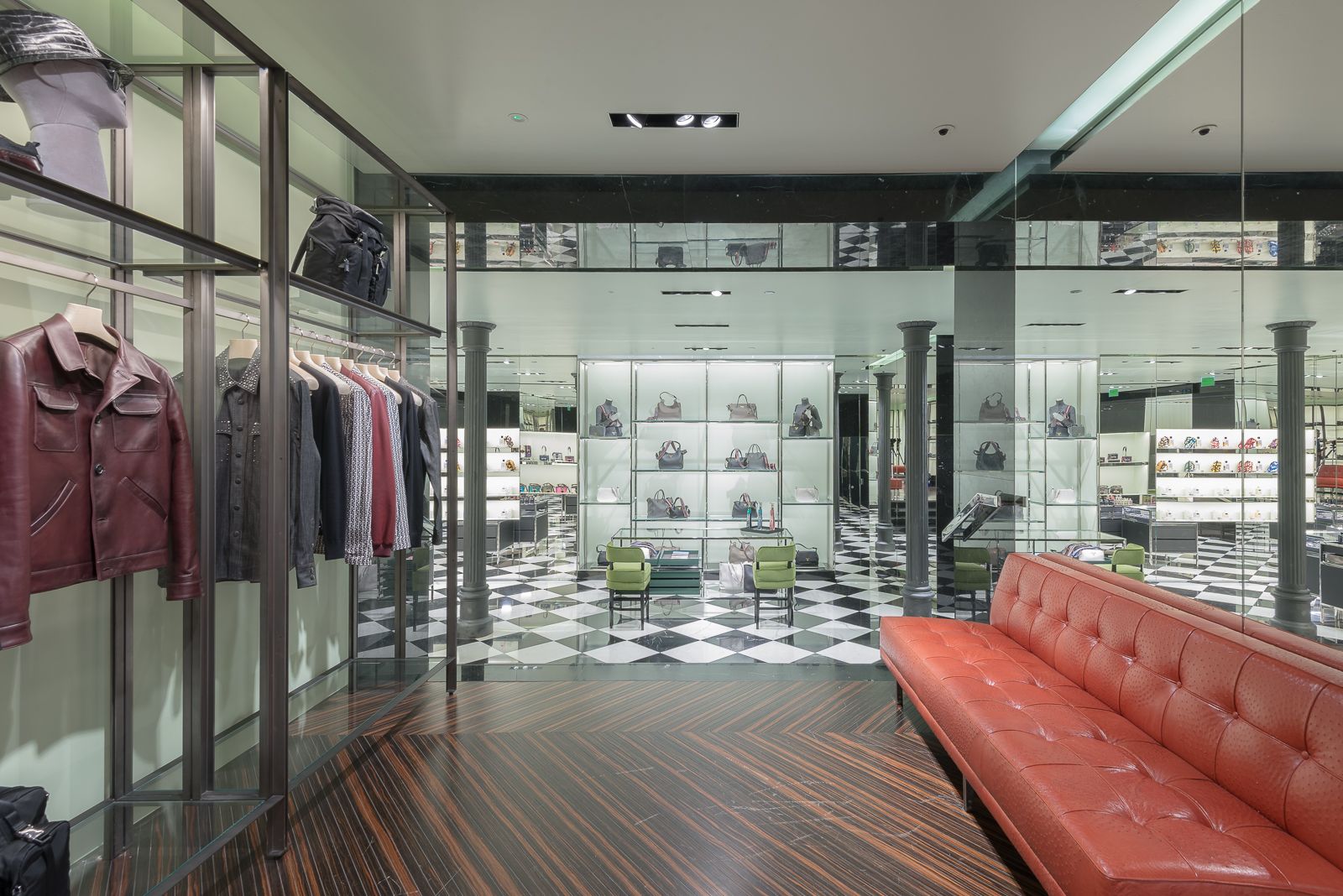 Prada store interior with clothing racks, leather jackets, and a checkered floor, featuring a red sofa and display shelves in the background.