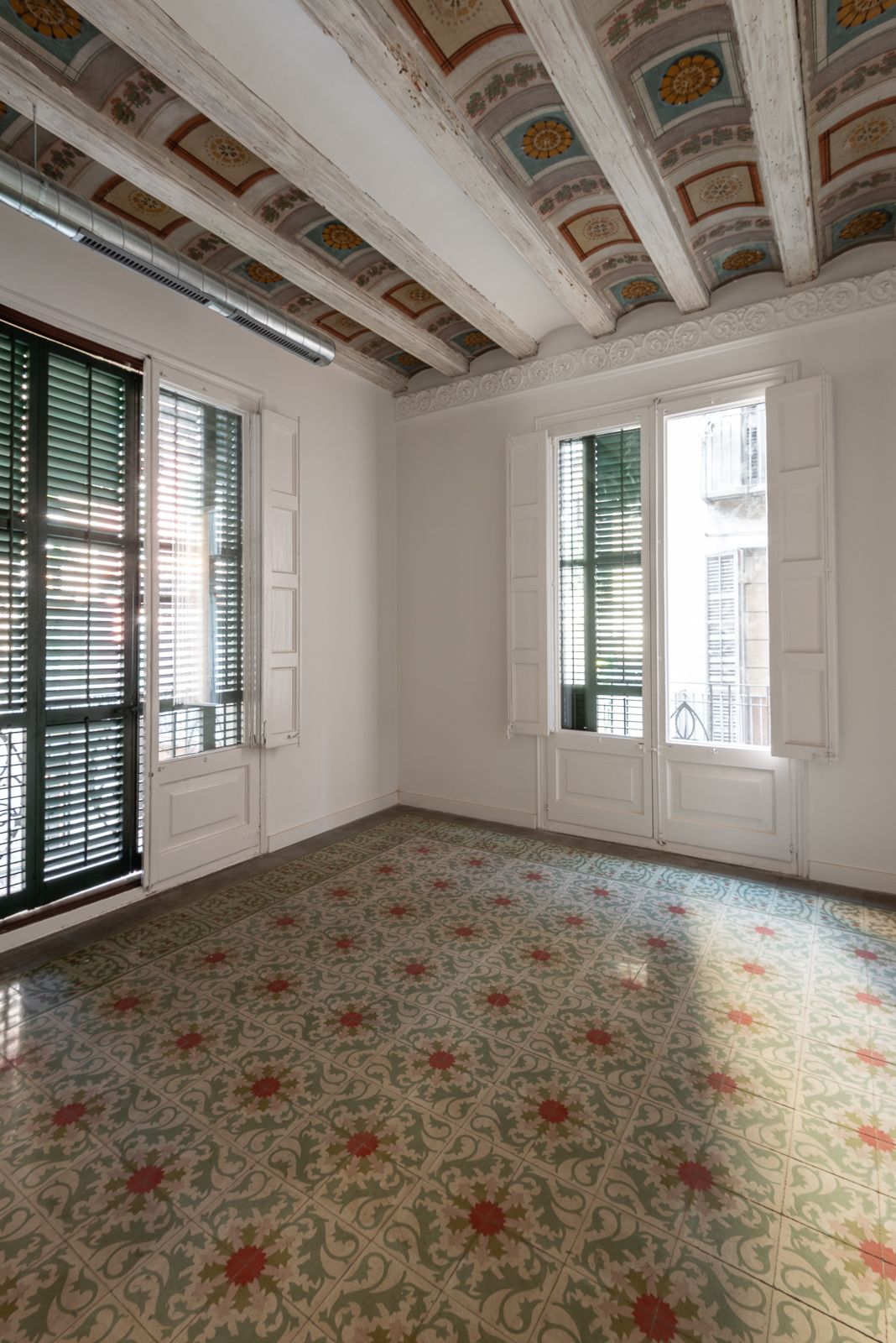 Room with patterned floor tiles, ornate beamed ceiling, and large windows with shutters.