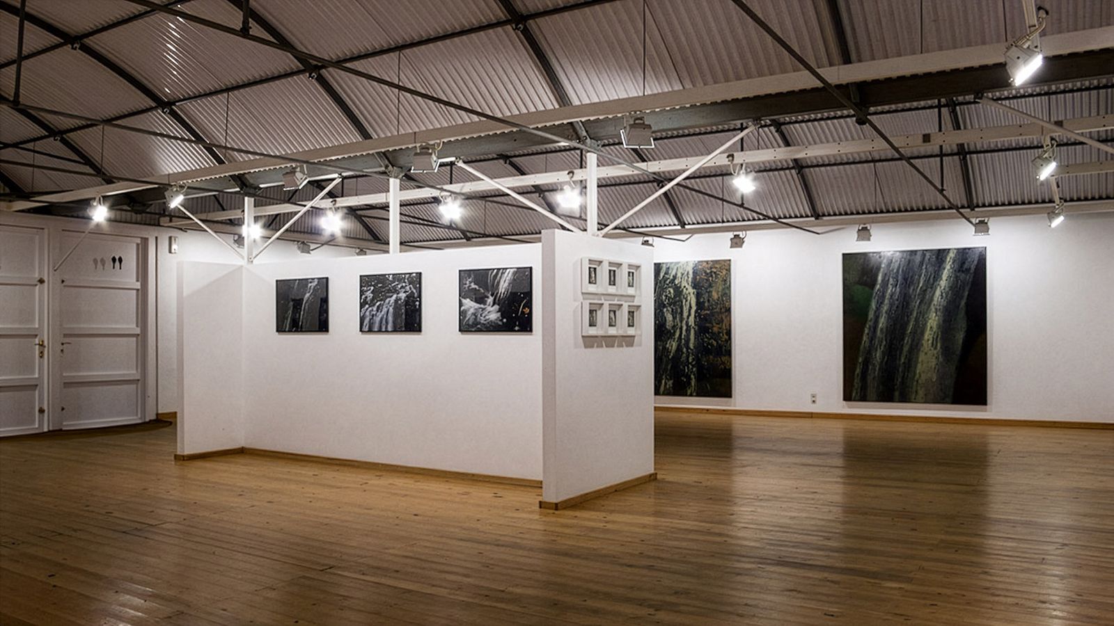 Galería espaciosa con obras de arte en las paredes, suelos de madera y techo metálico expuesto.