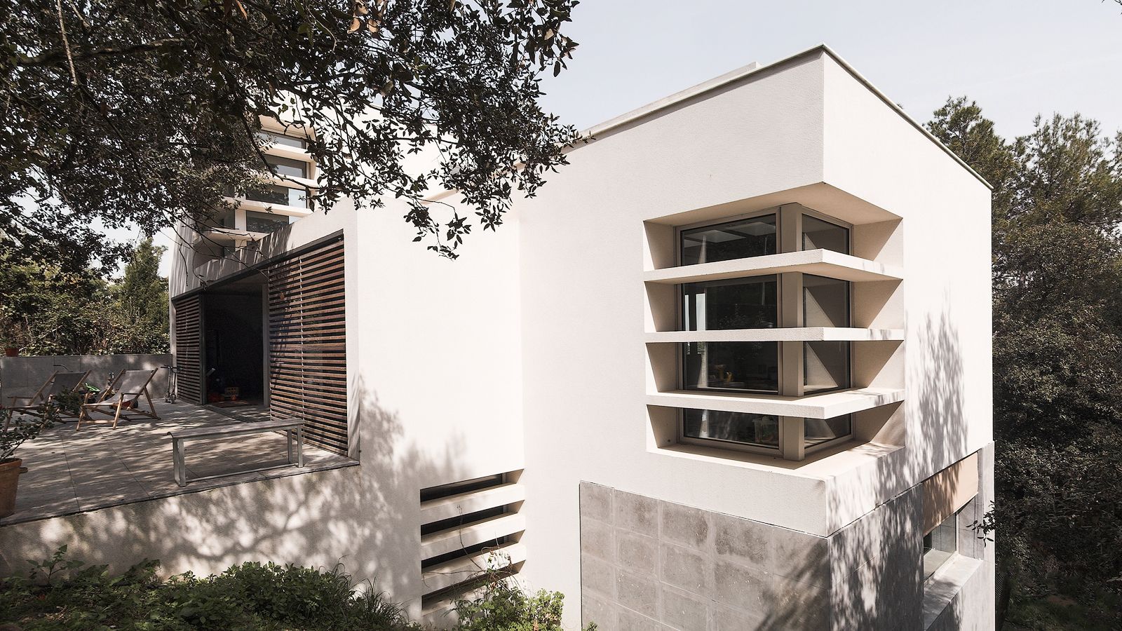 Exterior modern d'una casa amb grans finestres i una terrassa espaiosa, envoltada d'arbres i paisatge natural.