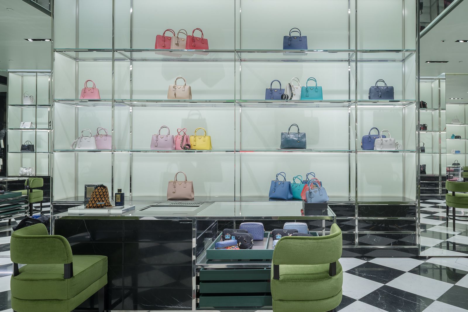 Elegant display of luxury handbags in a Prada store, with colorful bags arranged on glass shelves and green chairs in the foreground.
