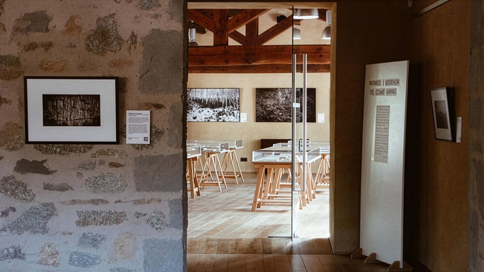 View into a gallery room with framed photos on the walls and display cases on wooden stands.