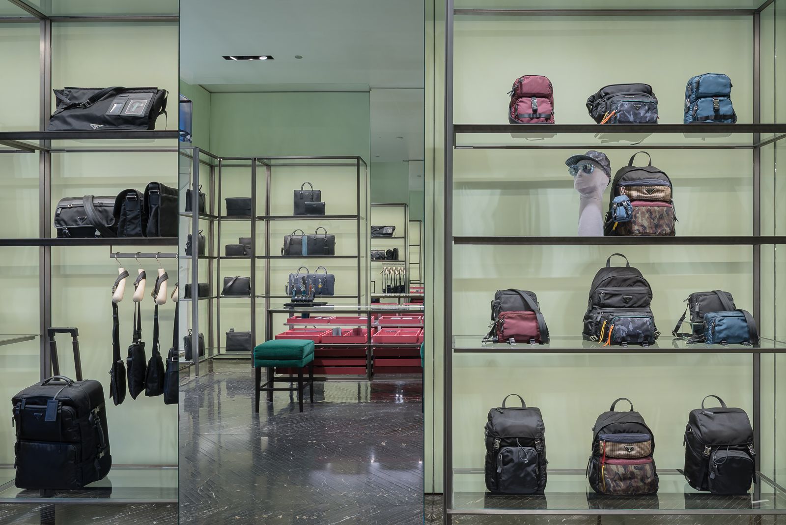 Luxury store interior with mirrors showcasing various designer bags and backpacks displayed on sleek metal shelves against a pale green backdrop.