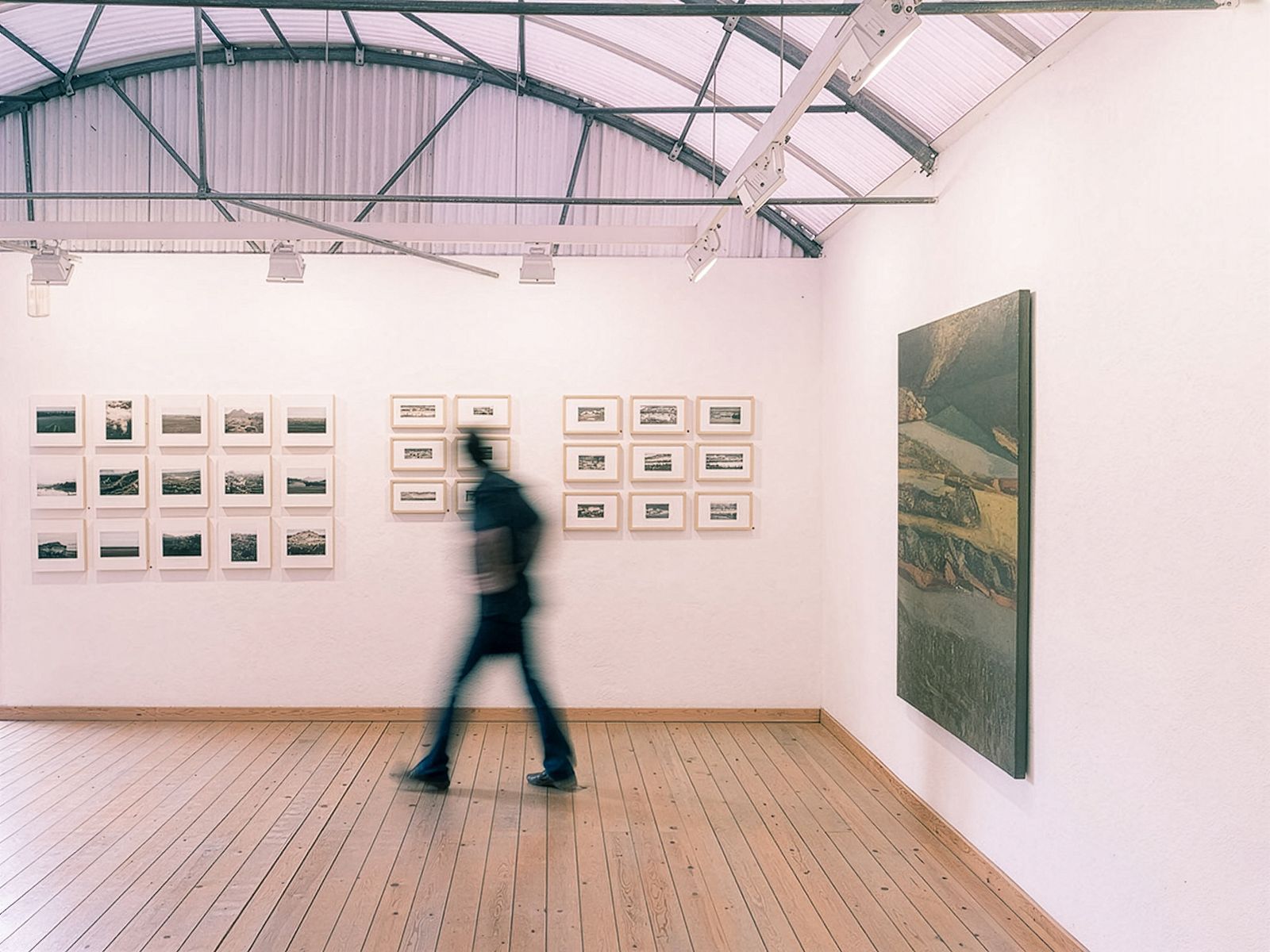 Vista de exposición con una persona caminando frente a obras de arte enmarcadas.