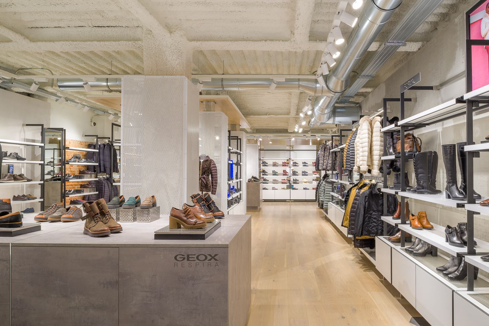 Interior de la botiga Geox mostrant una varietat de sabates i roba d'abric, amb un disseny de sostre industrial modern.