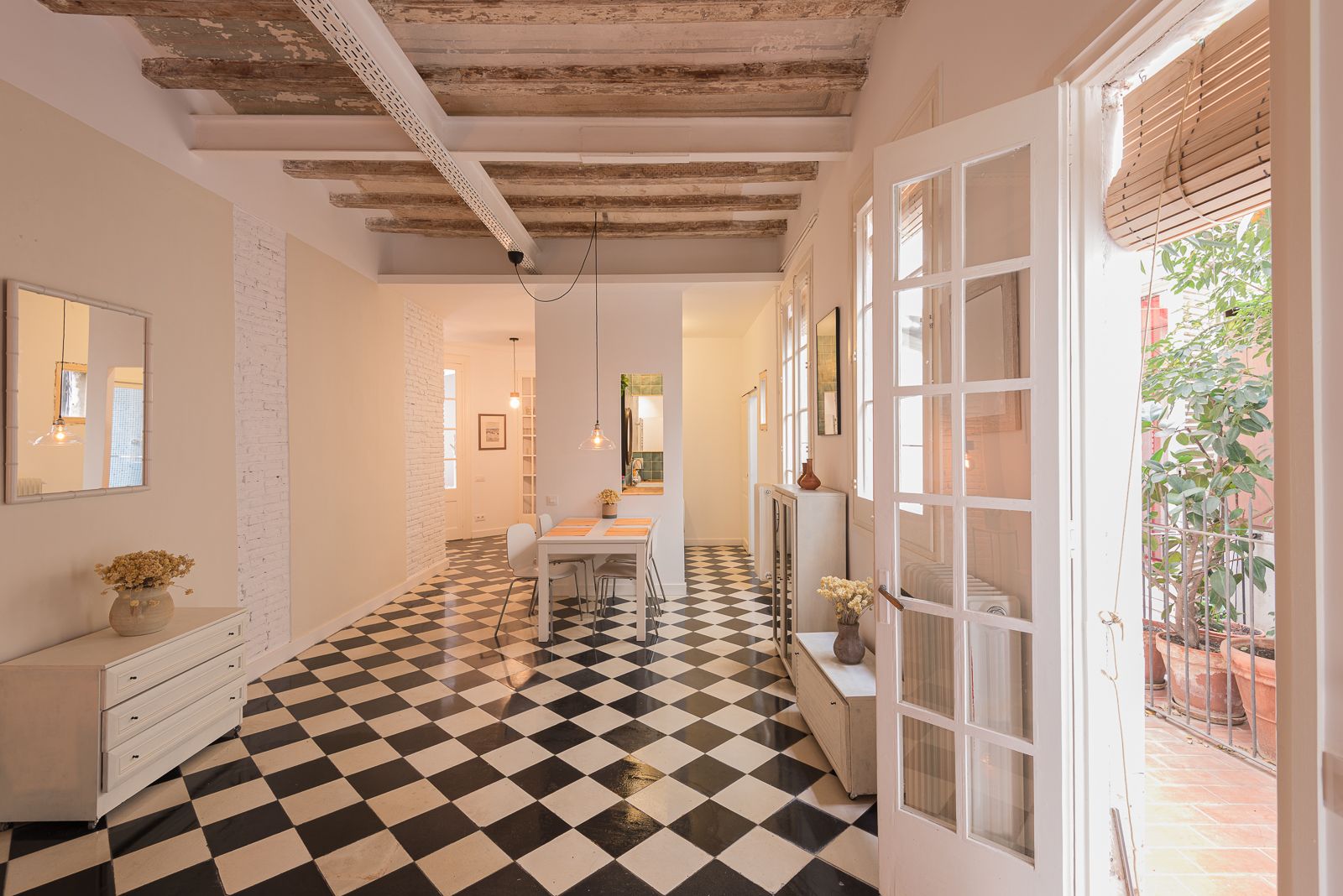 Zona de menjador espaiosa amb rajoles de terra de quadres, bigues vistes i portes franceses que s'obren a una zona de pati.